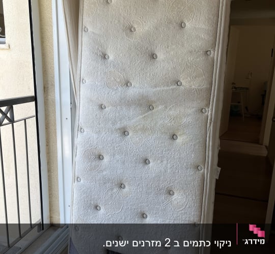מזרן עומד ליד חלון עם כיסוי לבן
